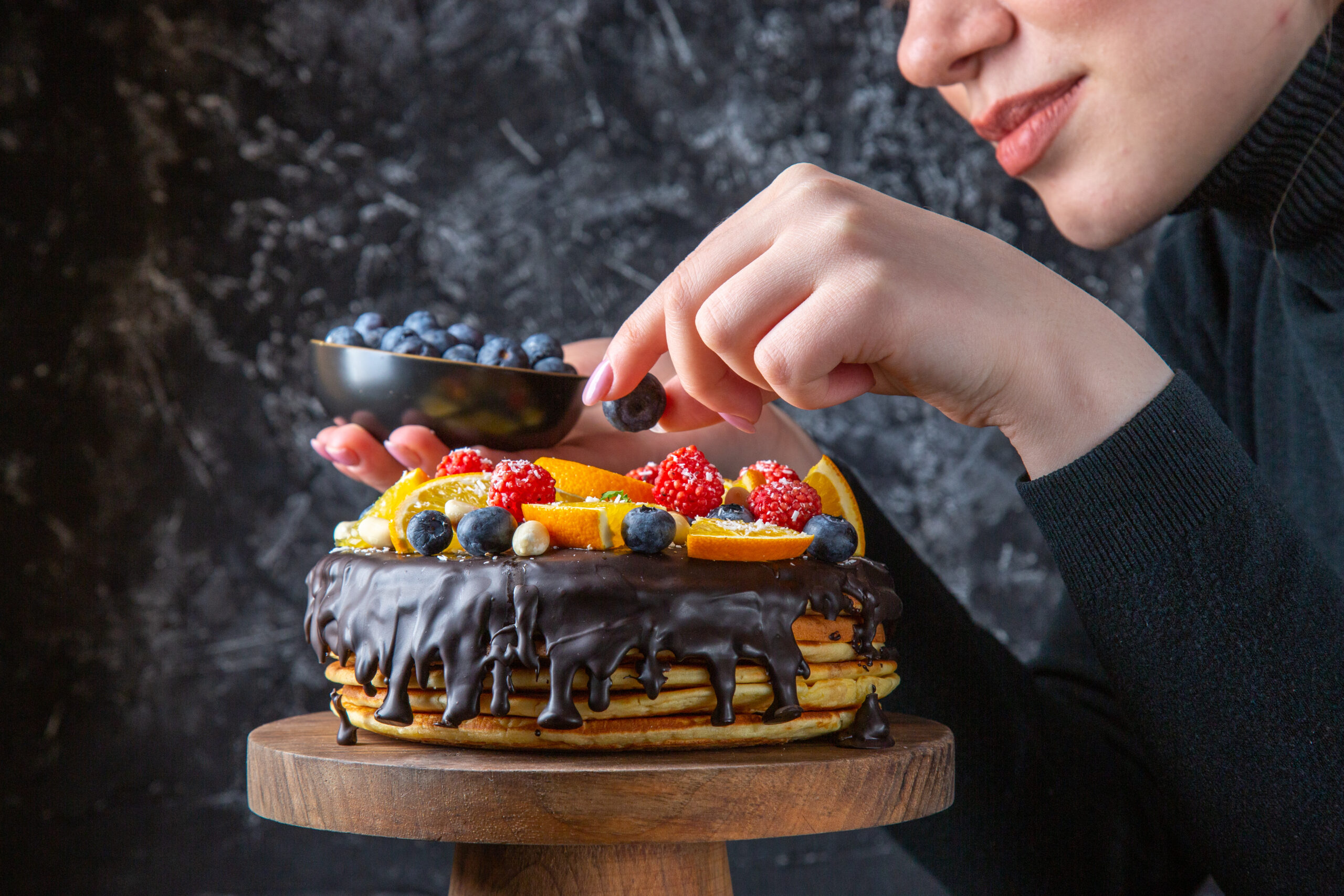 vkusnyi-sokoladnyi-tort-vid-speredi-ukrasennyi-fruktami-zensinoi-na-temnoi-stene